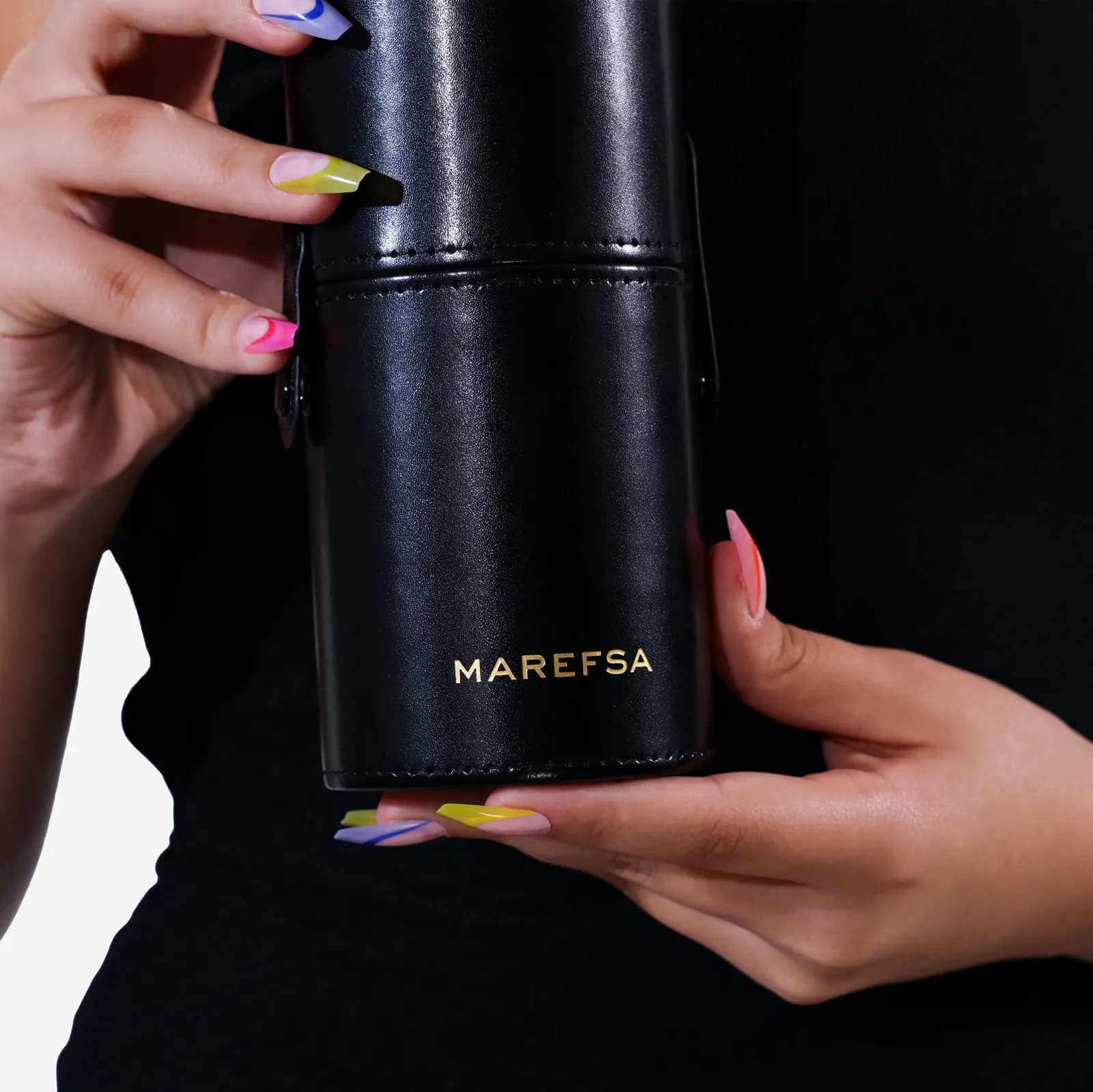 Hands holding the black MAREFSA travel case with its gold logo